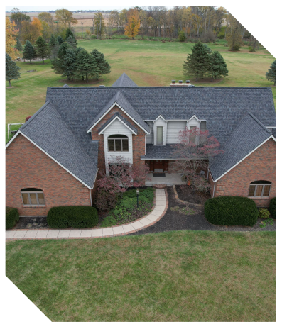 Aerial view of a large brick house with a sprawling lawn and trees.