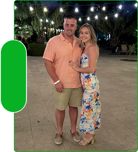 Couple posing under string lights with palm trees in the background.