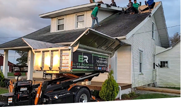 Roofers working on a residential home with a debris disposal trailer.