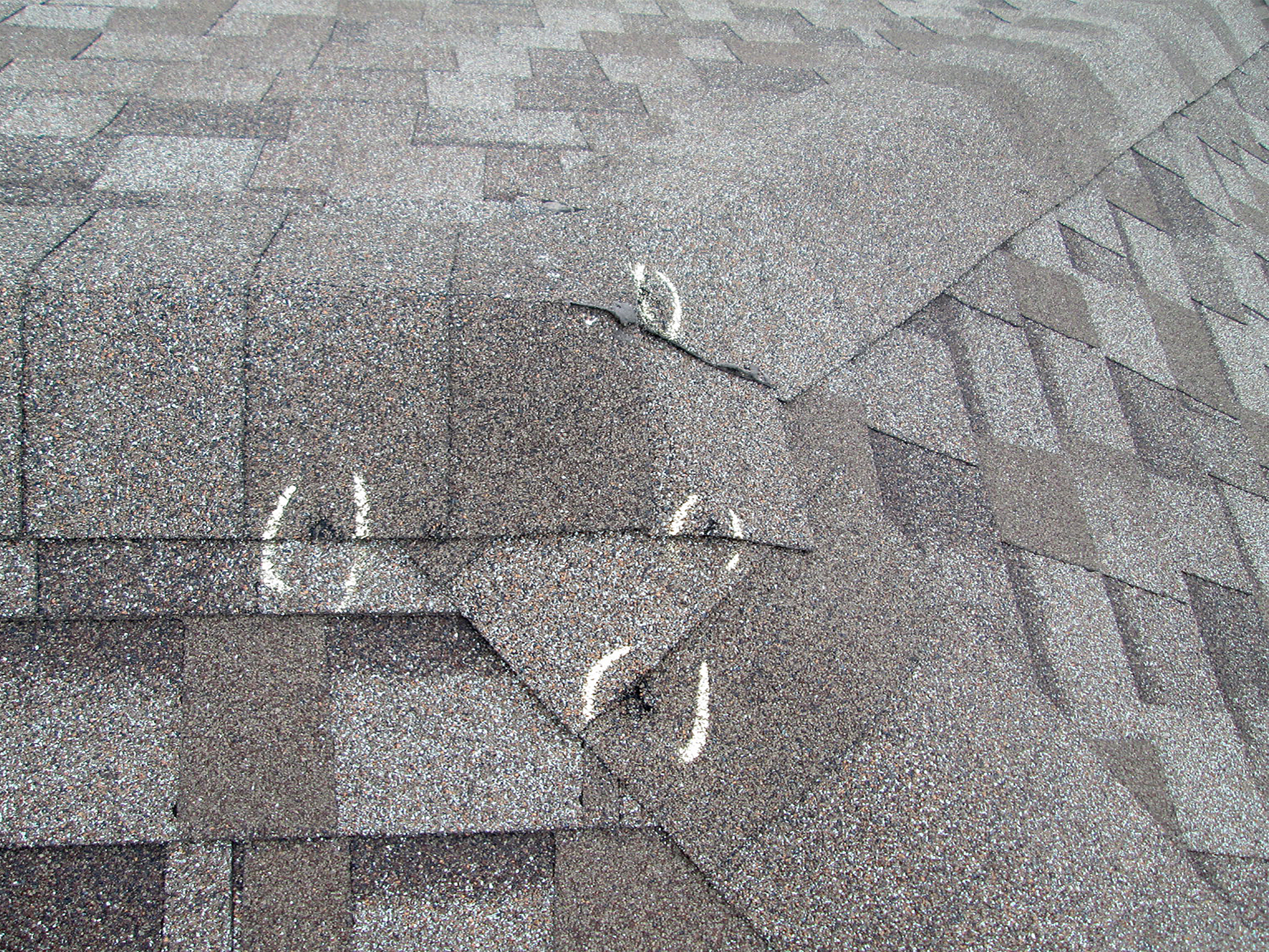 Close-up of a roof with visible hail damage marked in white chalk.